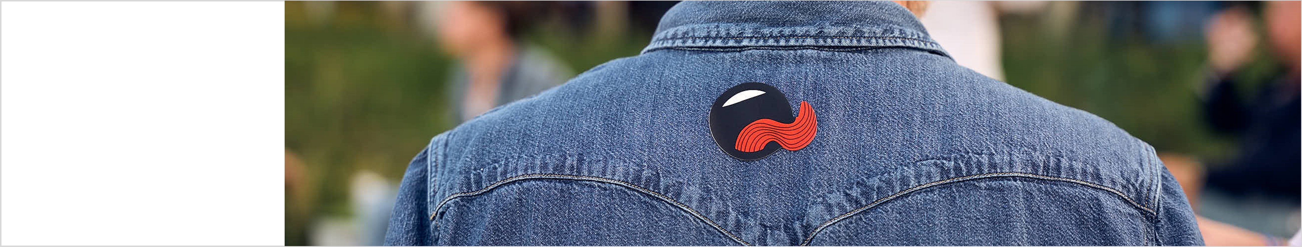 Back view of a person in a denim jacket with Open Mouth logo patch outdoors, blurred people in the background