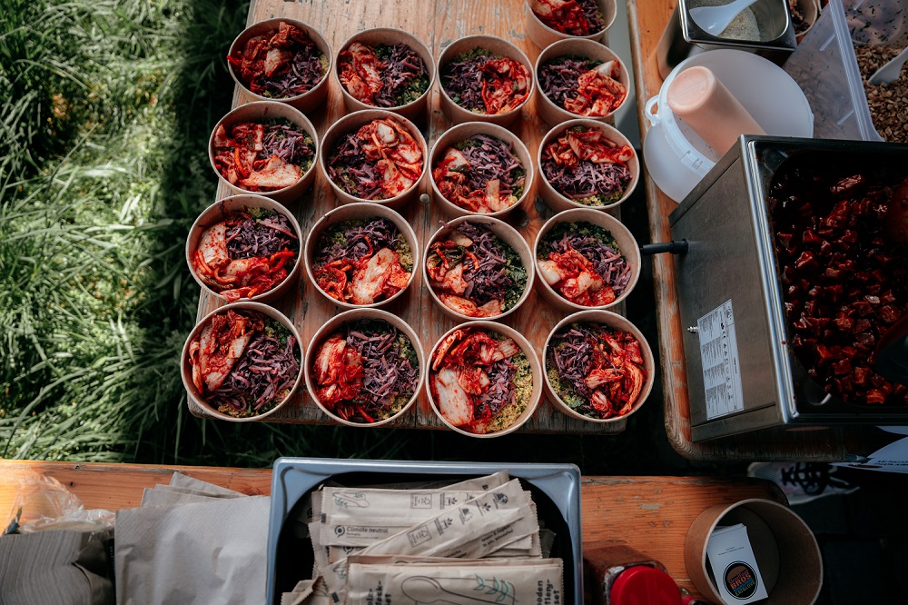 Top-down view of multiple serving bowls filled with colorful kimchi, red cabbage, and other fresh ingredients, arranged on a wooden table at an outdoor event during the OPEN MOUTH Hamburg Food Festival.