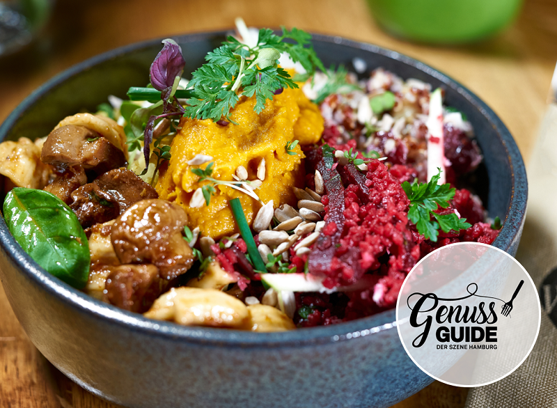 Close-up of a colorful bowl with pumpkin purée, beetroot, sunflower seeds, sautéed mushrooms, pasta, and fresh herbs – served in a dark dish. The logo of the Genuss Guide Hamburg is visible in the lower right corner.